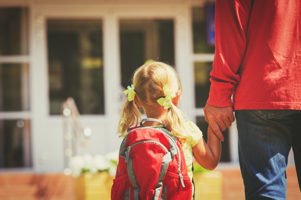 A child and caregiver walking hand in hand toward a welcoming daycare entrance